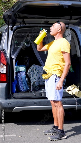 Healthy senior man drinking water from a reusable bottle, staying hydrated and taking care of his body during a sustainable road trip and active outdoor adventure