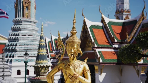 Golden Kinnara statue guards entrance to a temple at the Grand Palace complex. Ornate Thai architecture with pagodas and chedis
