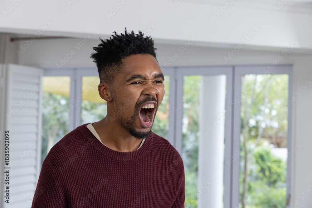 Obraz premium African American man standing in bright living room near glass doors, shouting and wearing sweater