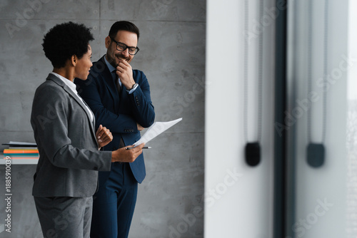 Photos Professional African American businesswoman and Caucasian businessman standing and talking in a modern office with plenty of copy space