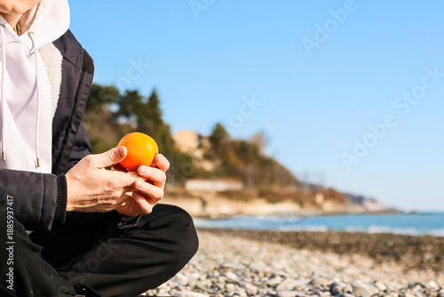 Schilderij op canvas Hand Holding Fresh Orange on Pebbly Beach