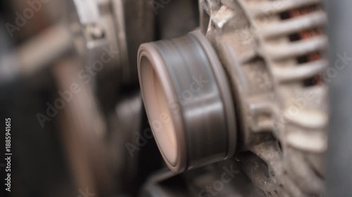 Close-up view of a car alternator and drive belt mechanism rotating while the engine is running, showing the mechanical power transmission and electricity generation for the vehicle