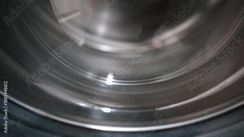 Detailed close up of a shiny stainless steel washing machine drum spinning rapidly during the laundry cycle, showing the metallic surface reflecting light and motion in a continuous loop