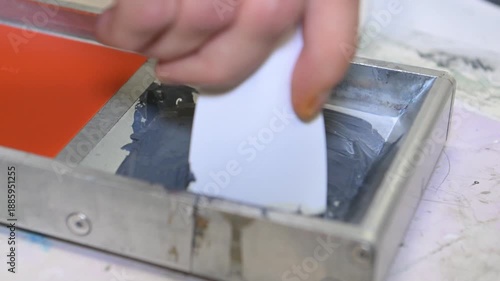 A man's hand mixes the ink in a silkscreen printing box in the workshop of a printing company