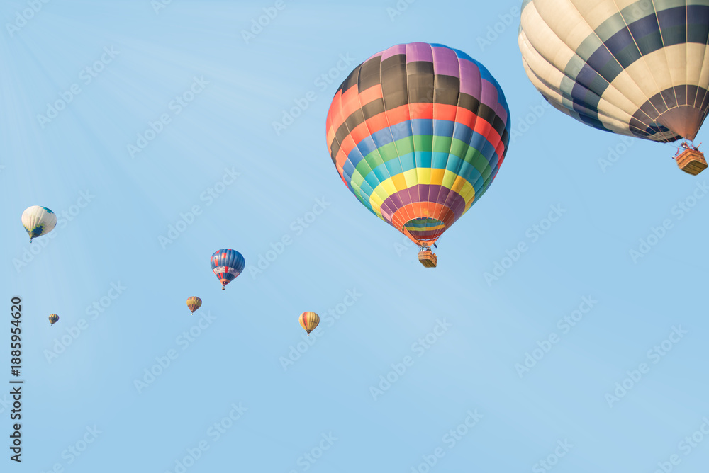 Fototapeta premium Vibrant rainbow-patterned hot air balloon leading a group across a bright blue sky.