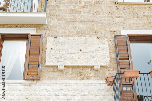 Bari, Italy. Stone facade along Via Venezia in Bari with windows and balconies, featuring a commemorative marble slab marking the Miracle of the Fire dated May 8, 2003.