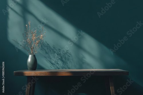 Dried flowers in vase standing on wooden table against petrol wall with window light creating shadows