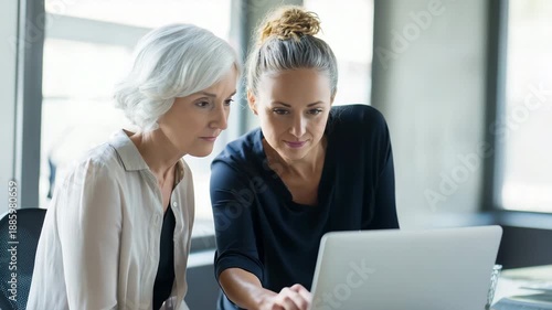 senior mentor coaching a junior colleague while reviewing work on a laptop in office, supportive mentoring vibe, focused attentive expressions 