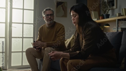 Devastated young woman with rosary looking down and sharing her feelings with mature spiritual guide who holding bible book and carefully listening