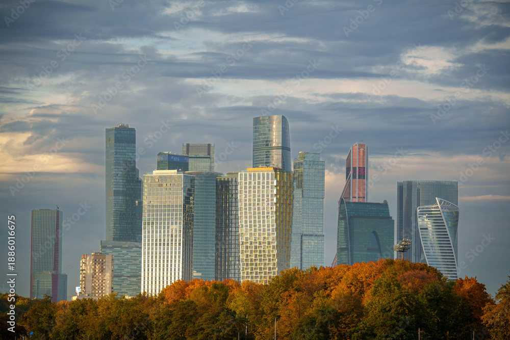 Obraz premium Moscow City skyscrapers with colorful autumn trees and cloudy sky.Close-up of Moscow City skyline with modern skyscrapers rising above autumn trees