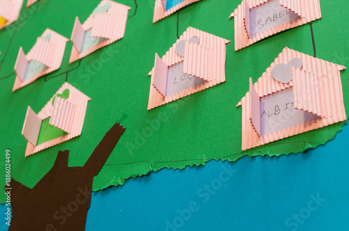 Detail of a handmade genealogy project showing pink corrugated paper houses with flaps opening to show names