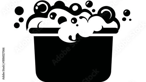A simple, black and white icon of a bucket overflowing with bubbly suds and floating bubbles