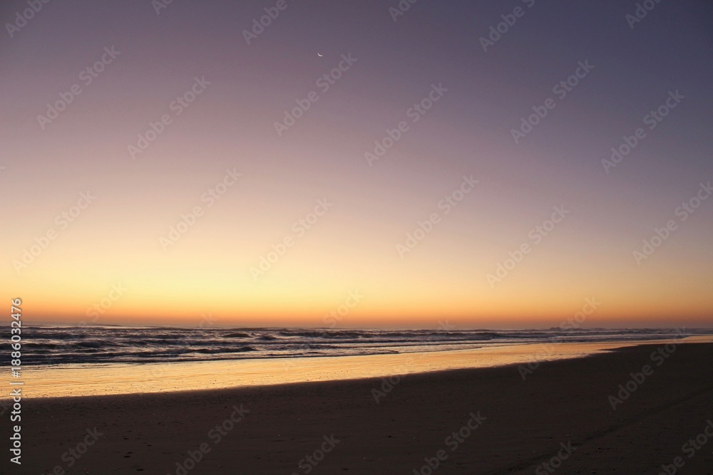 Obraz premium Peaceful Ocean Sunset with Crescent Moon and Gentle Waves