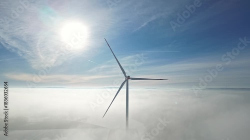 Wind turbine stands tall above the clouds, illuminated by sunlight, showcasing the vast sky and foggy landscape in a serene and tranquil environment