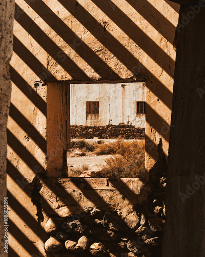 Juego de luces y sombras proyectadas sobre una estructura en ruinas, creando patrones geométricos y una atmósfera cálida y misteriosa en un entorno arquitectónico abandonado.
