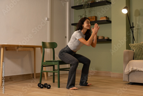 Fotografía Smiling athletic woman performing chair squat exercise at home using bodyweight