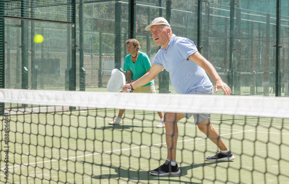 Fototapeta premium Elderly man and adult man in doubles playing paddle tennis on tennis court