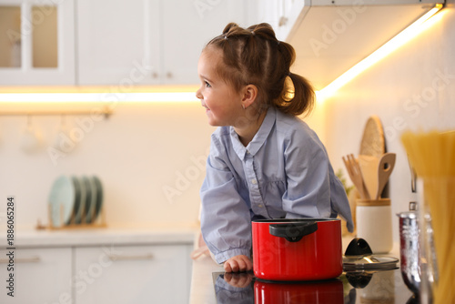 Child safety at home. Little girl playing with pot on stove in kitchen, space for text