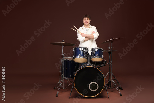 Smiling teenage boy with drumsticks and drum kit on brown background, space for text