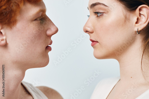 Canvas Print Portrait of young man and woman facing each other with calm expression closeup on light background, showing natural skin and facial features in detail