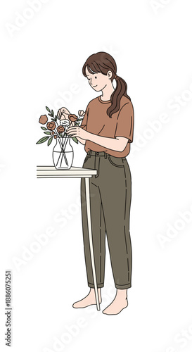 Young woman arranging flowers in vase while standing by table  