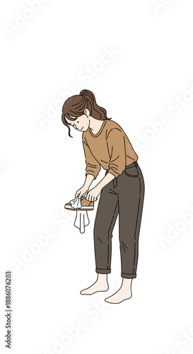 Woman cleaning shoes while standing barefoot on white background  