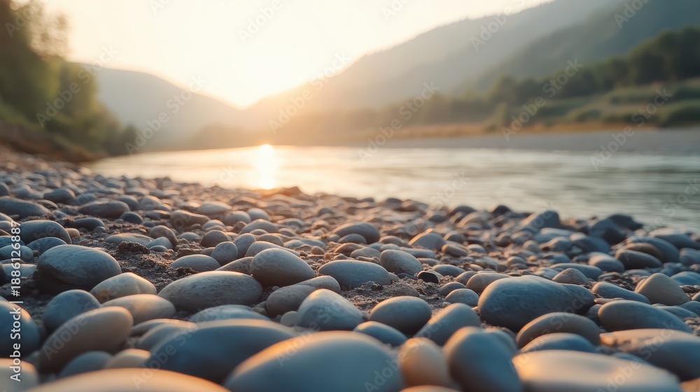 Fototapeta premium Smooth grey river stones forming a subtle mosaic pattern on a serene beach with mountains and golden sunset in the background