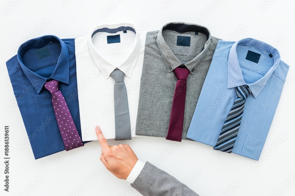 Fototapeta premium Four men's dress shirts with ties: blue with polka dot tie, white with gray tie, gray with burgundy tie, light blue with striped tie. Hand pointing at shirts. Men's fashion, top view.