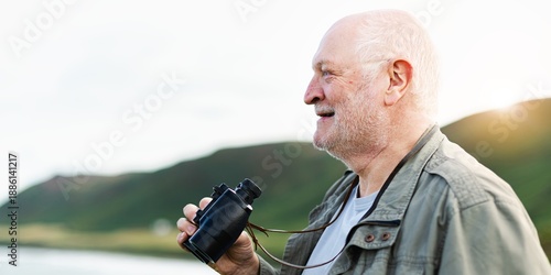 Elderly white man holding binoculars, enjoying nature. Senior man with binoculars, smiling. Elderly man, nature, binoculars, outdoors nature. Senior birdwatcher using binoculars and birdwatching.