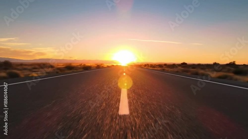 A long straight asphalt road extends into the distance at sunset centered on a bright sun above a desert landscape with sparse vegetation and distant mountains