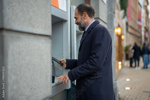 Photos Mature man using atm with smartphone for transaction