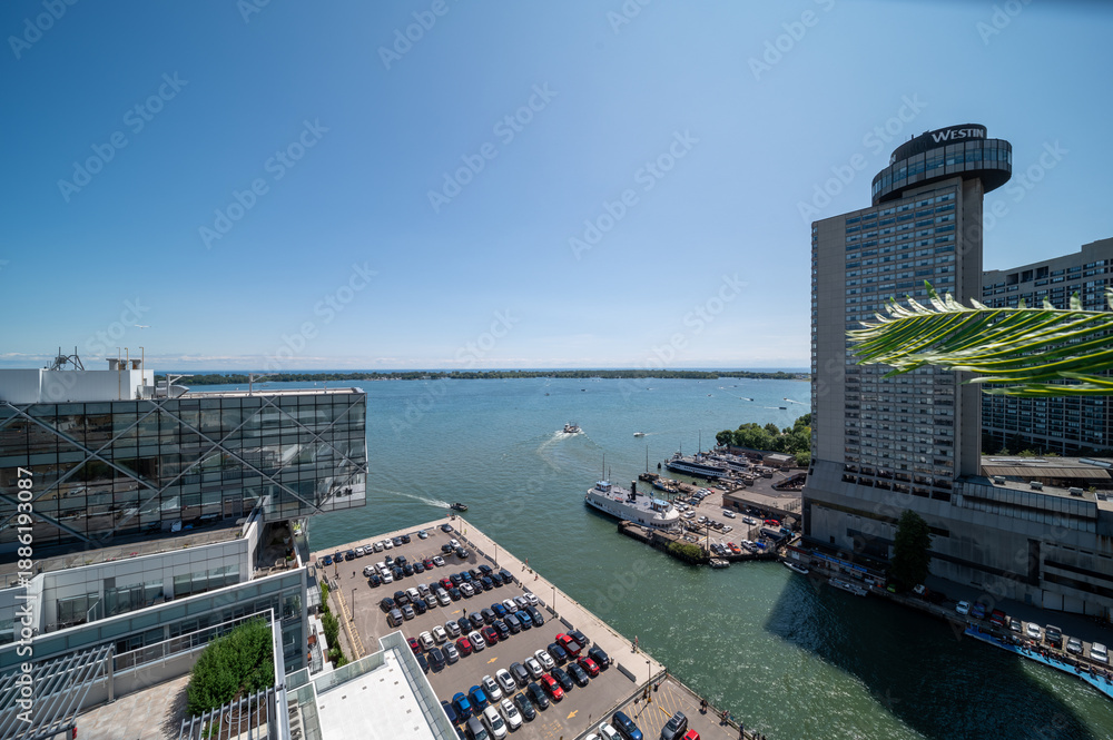 Fototapeta premium Elevated view of toronto waterfront and harbor on a sunny summer day, boats navigating lake ontario beside high rise city skyline, marina and busy parking lot visible