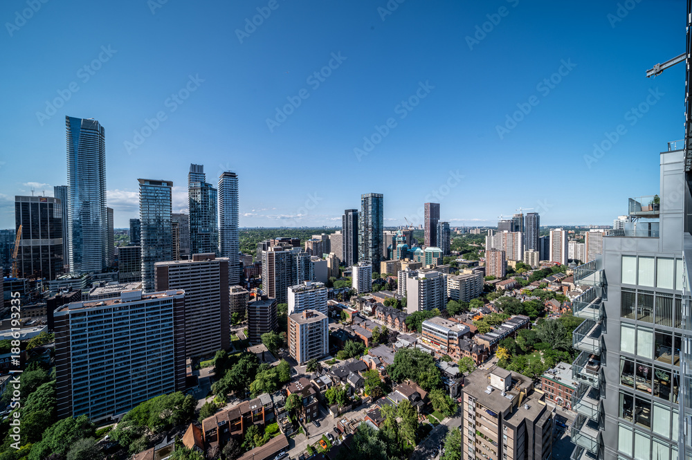 Fototapeta premium Toronto's urban landscape blends modern high rise architecture with residential neighborhoods and green spaces under a clear blue sky, illustrating city growth and diverse living environments
