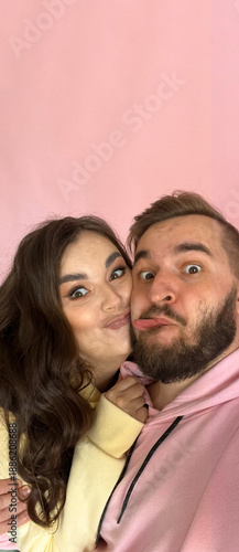 Vertical mobile photo banner. Young adult man with beard in pink hoodie and mature woman in yellow sweatshirt looks at camera, smiles, sticks out tongue. Concept of Valentine day, 14 february, love