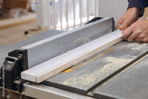 Worker is using table saw to cut piece of wood dust is visible on table surface on carpentry work.