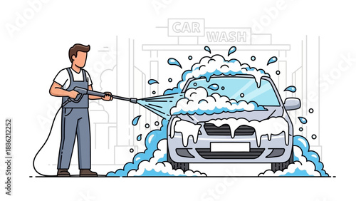 A man in blue overalls using a pressure washer to thoroughly clean a silver car covered in white soap suds at a car wash station.