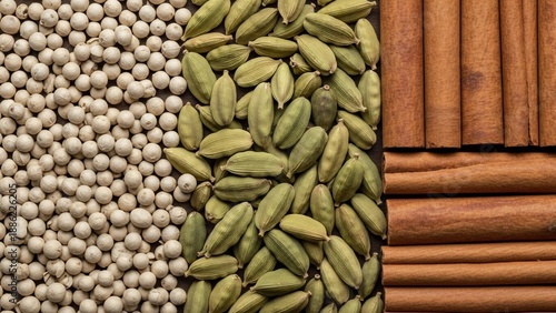 Close-up overhead view of three distinct sections of aromatic spices: white peppercorns, green cardamom pods, and cinnamon sticks.
