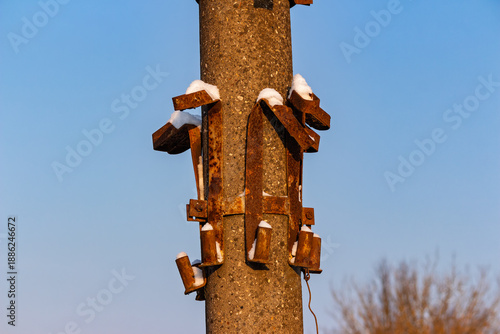 Wallpaper Mural Close-up of a heavily rusted metal bracket assembly on a concrete utility pole, dusted with small patches of white winter snow against a clear blue sky in January sunlight Torontodigital.ca
