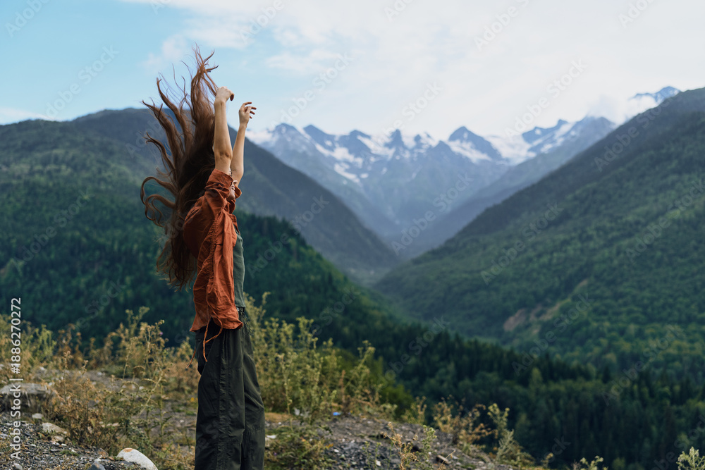 Fototapeta premium A person stands on a rocky overlook in a vast mountain landscape with arms raised, embracing freedom and adventure, capturing a triumphant moment and a strong connection with nature