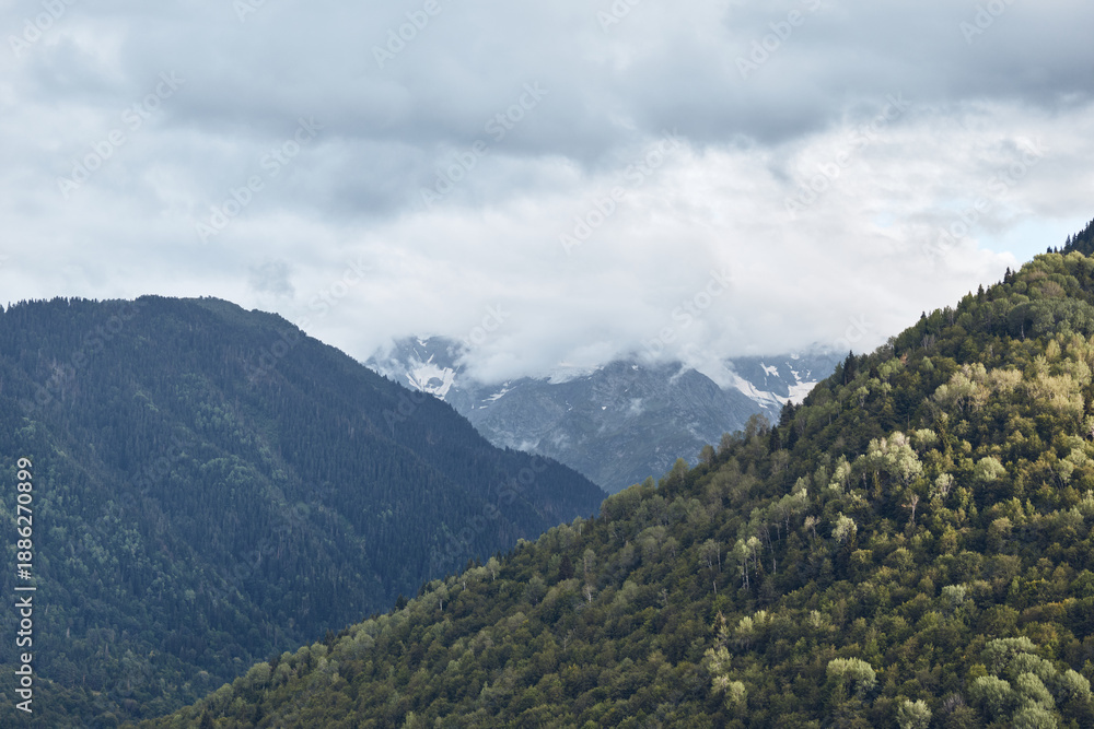 Naklejka premium Majestic mountain landscape with forested slopes and a cloudy sky over rolling hills, presenting a tranquil natural scene ideal for nature and travel themes.