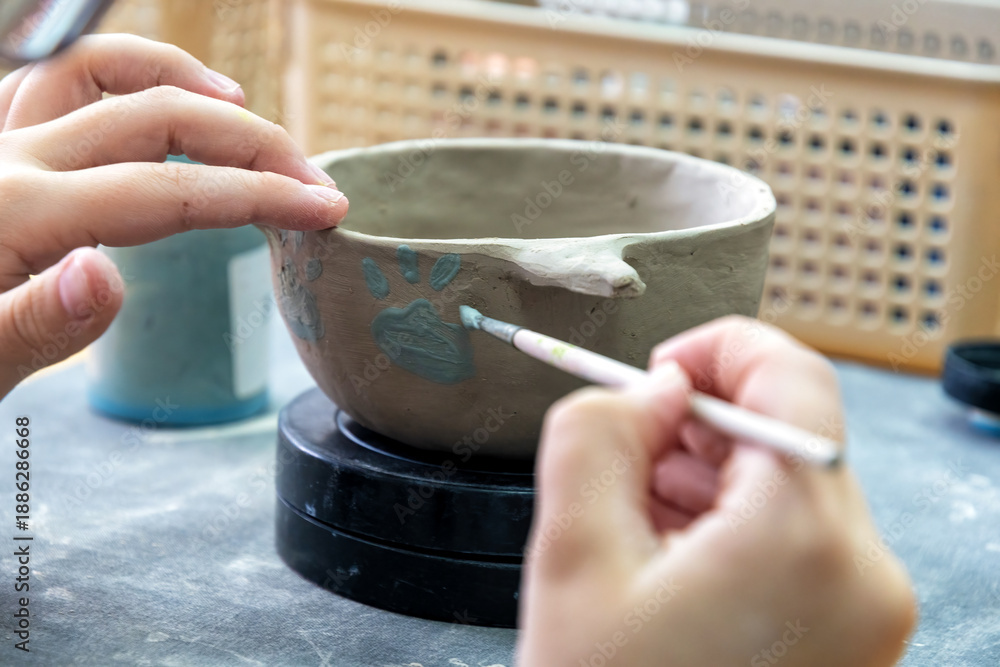 Obraz premium Child's hands carefully paint a handmade clay pot with paw print design. Creative art workshop activity, fostering development and education