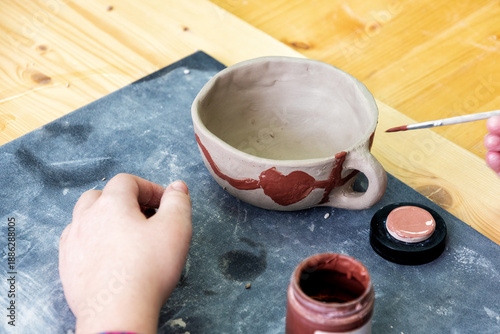 Hand painting a unique, handmade clay cup with terracotta paint in a pottery workshop. Capturing creativity, learning, and artistic skill