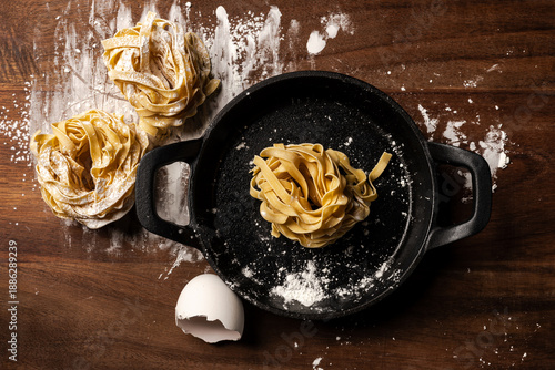 Tableau sur toile fresh homemade tagliatelle pasta nest arranged in a black pan on a rustic wooden