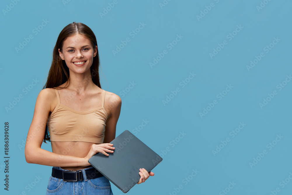 Obraz premium smiling young woman holding laptop, casual outfit, blue background, happy expression, technology, lifestyle concept