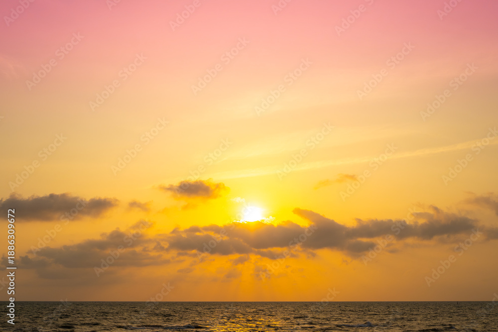 Fototapeta premium Nature sky breathtaking golden sunset over a calm ocean, with the entire sky and water bathed in brilliant shades of yellow and orange. Streaky clouds enhance the dramatic display of light 
