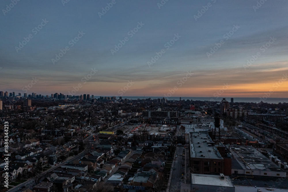 Fototapeta premium Panoramic aerial view capturing the toronto city skyline and residential areas transitioning into dusk, with vibrant sunset colors painting the horizon above lake ontario