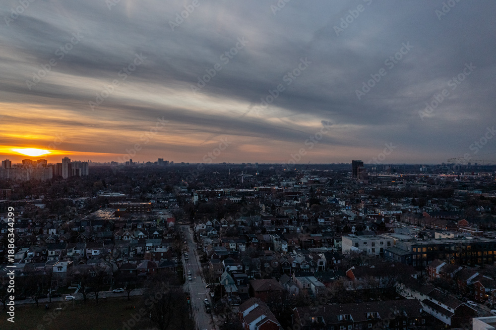 Obraz premium Cityscape view over residential housing and urban sprawl in toronto, ontario, canada, with a dramatic cloudscape catching the golden hour light during sunset
