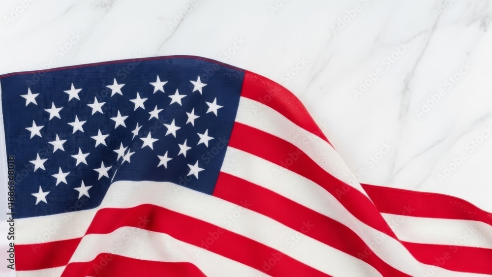 Obraz premium American flag draped on white marble surface. Close-up of stars and stripes waving gently against a clean, modern backdrop. Patriotic symbol with copy space.
