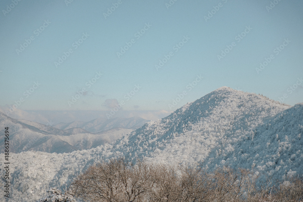 Obraz premium Wide winter mountain range on Mt Gyebangsan, South Korea, covered in pristine snow under a clear blue sky, offering an open, minimal landscape