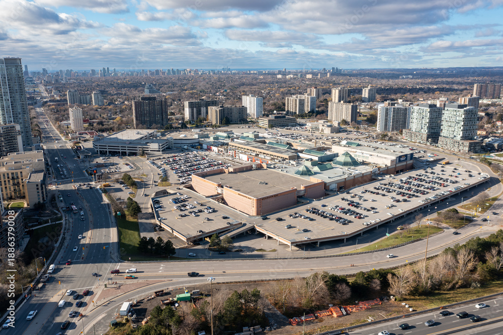 Obraz premium Aerial view capturing a large urban shopping mall surrounded by multi level parking lots and busy roads, with residential high rise buildings and toronto's skyline in the distance